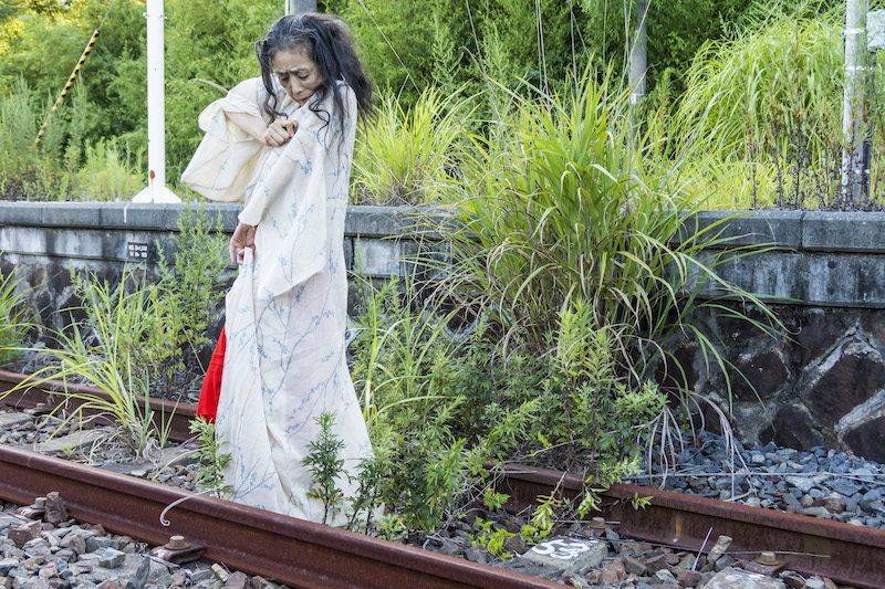 Eiko walks on the railroad tracks in Fukushima, she pinches her robe at the shoulder